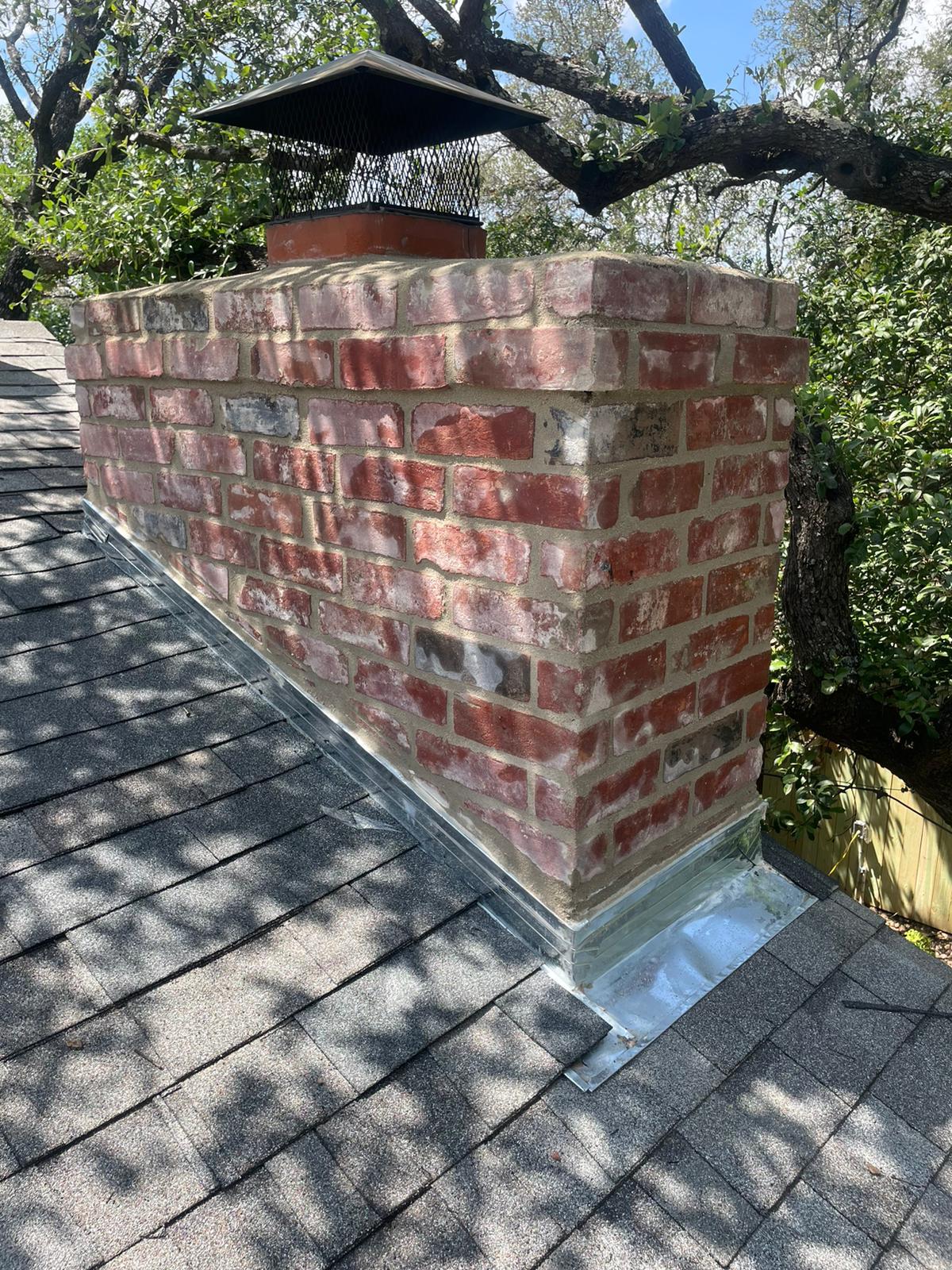 Red brick chimney with new black chimney cap and step flashing