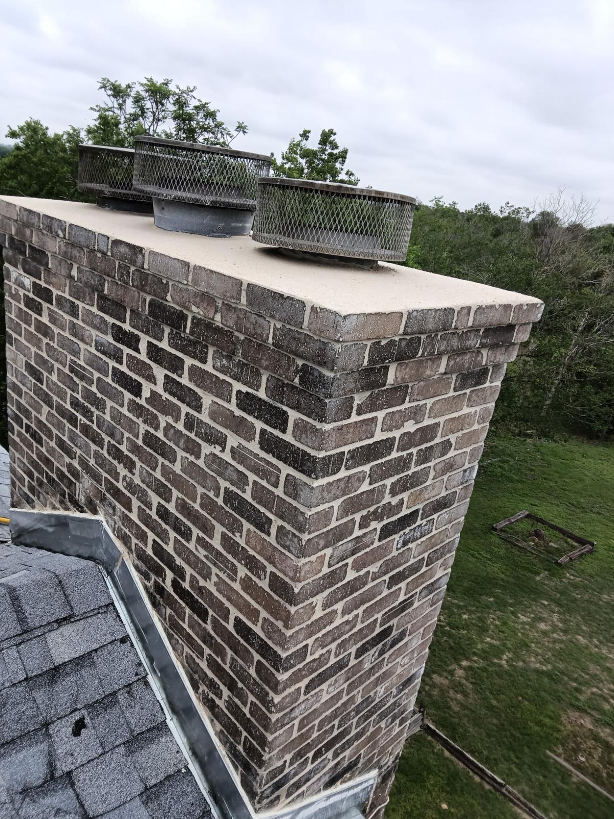 Brick chimney with freshly coated crown and mesh flue caps