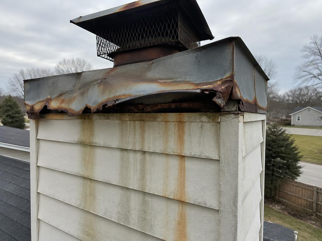 Rusted and warped chimney chase cover with rust stains on siding before replacement